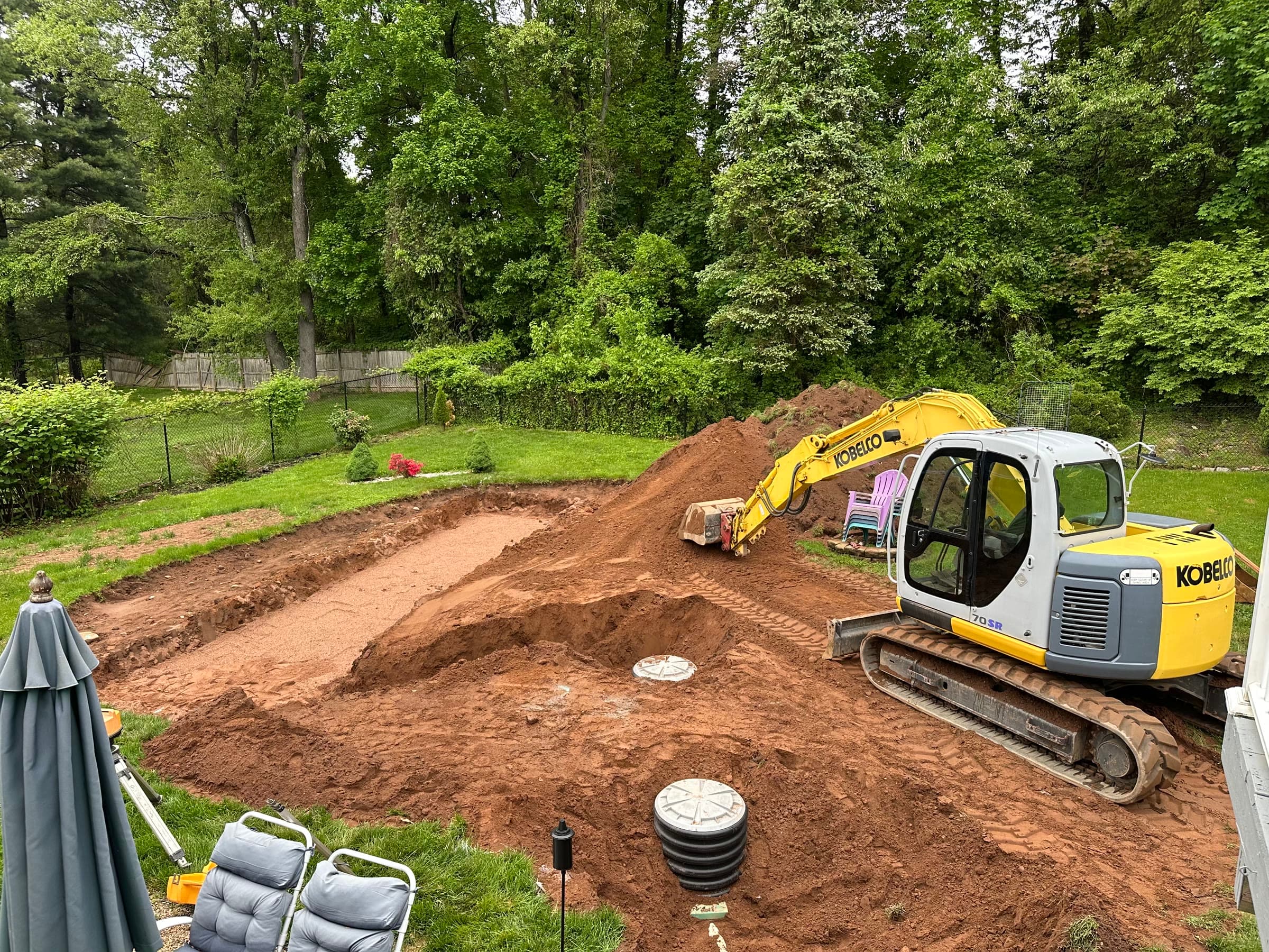 Septic system backfilled, tank and pump-chamber lids in, Kobelco excavator on the fill.