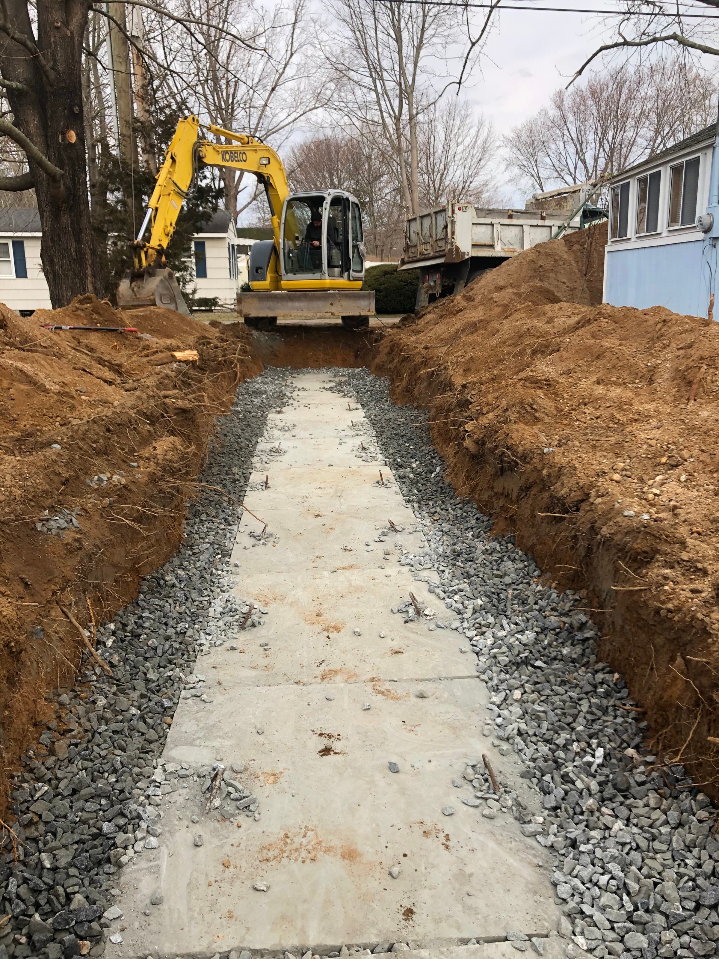 Concrete gallery septic system bedded in gravel, with an excavator on the spoil pile.