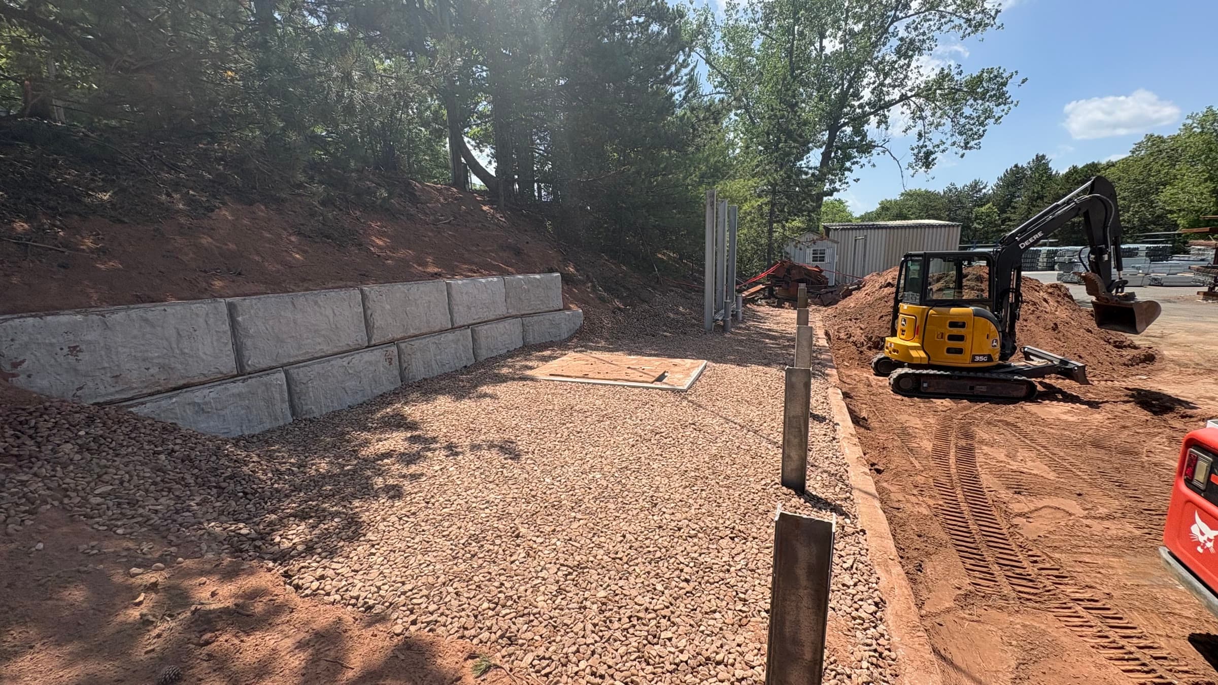 Utility install and block retaining wall with a gravel pad and compact excavator.