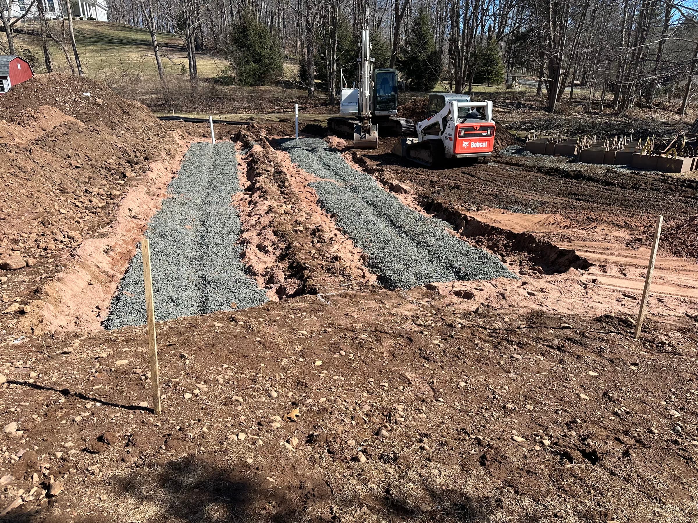 GST leaching system: parallel stone-filled trenches with a skid steer at the head of the field.